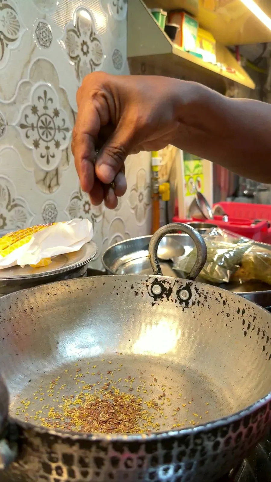 Seeds sprinkled by hand into an iron kadai